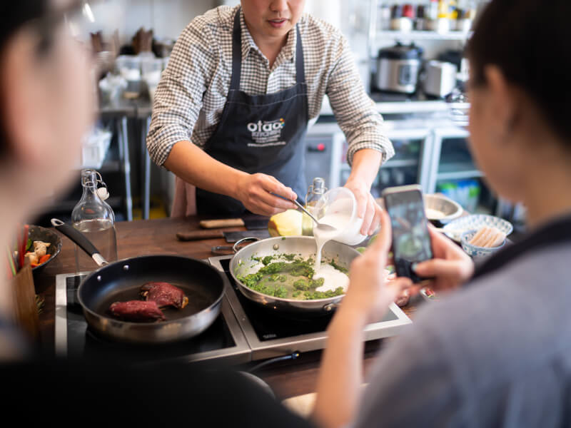 Person adding white liquid to a steel skillet full of green paste