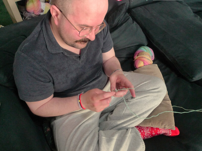 Man sitting cross legged on a sofa crocheting