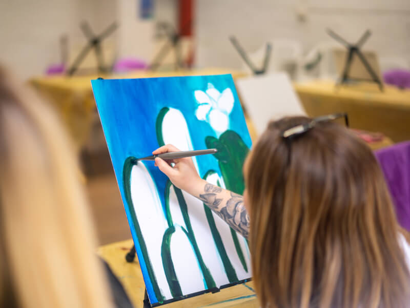 A close up of a person painting a blue and green picture on a canvas