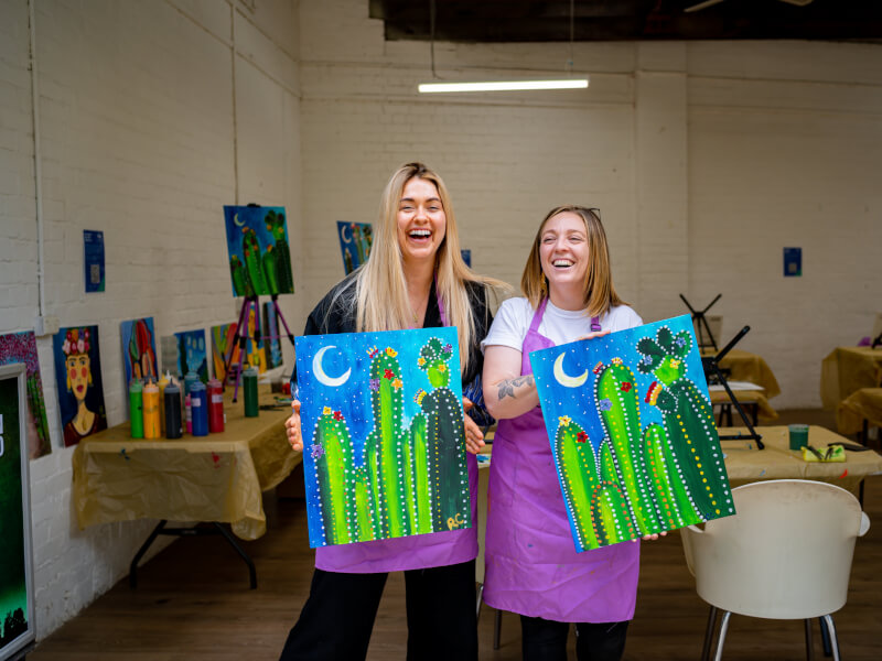 Two girls show off the paintings they made in a paint and sip class.