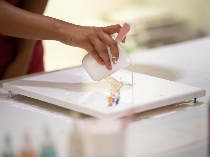 A hand pouring pant onto a canvas.
