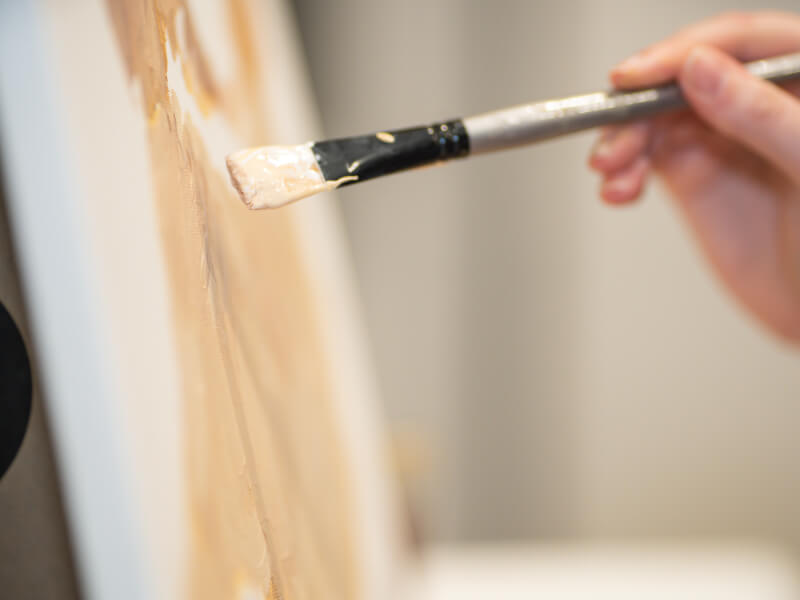 A close up of a hand learning to paint a dog with beige acrylic apint.