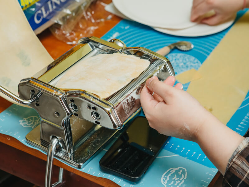 Hands working on a pasta machine in a pasta making workshop