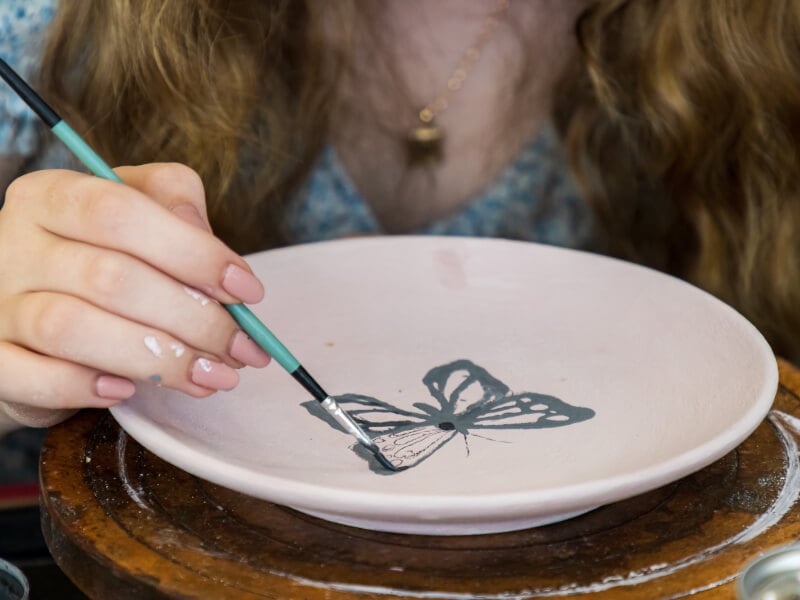 A woman decorates a plate with a butterfly in a pottery painting class.