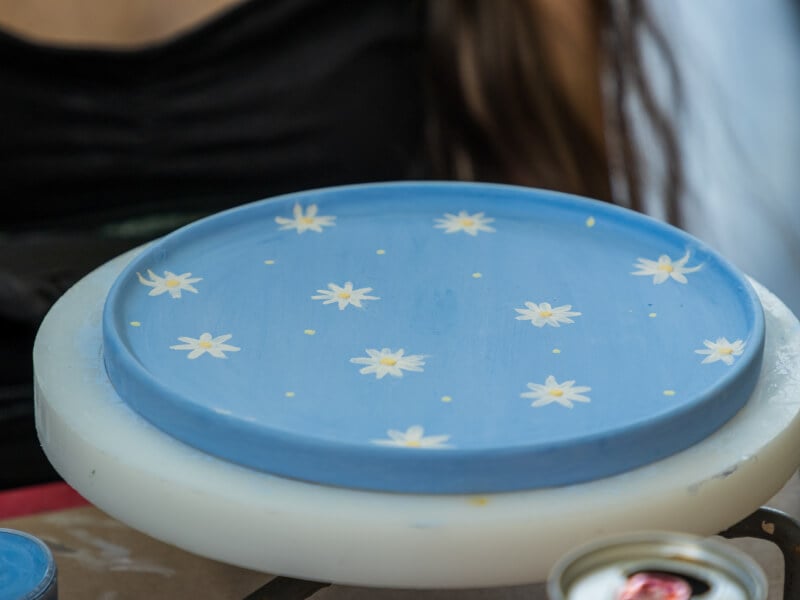 A finished painted ceramic piece of a blue plate covered in white flowers.