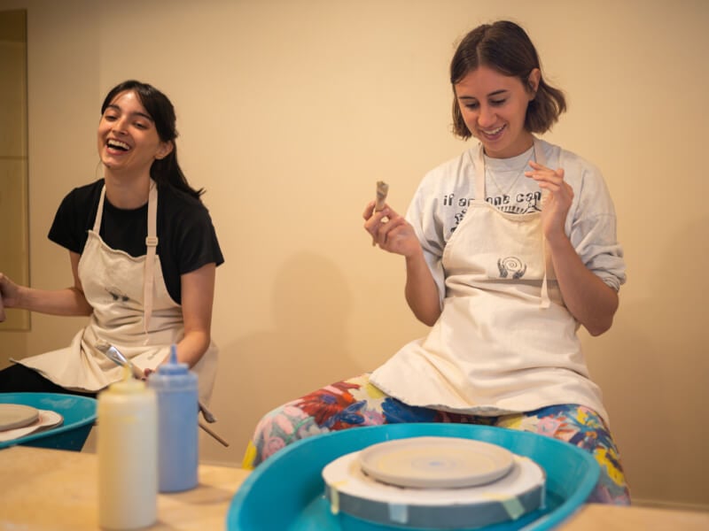 Two women smiling and laughing at a pottery class.