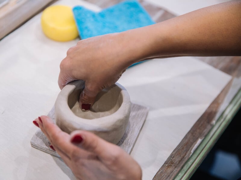 A person moulds clay with their hands at a pottery class.