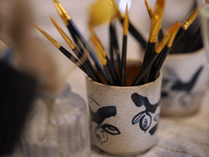 A pot handpainted with a blue floral design, holding paintbrushes