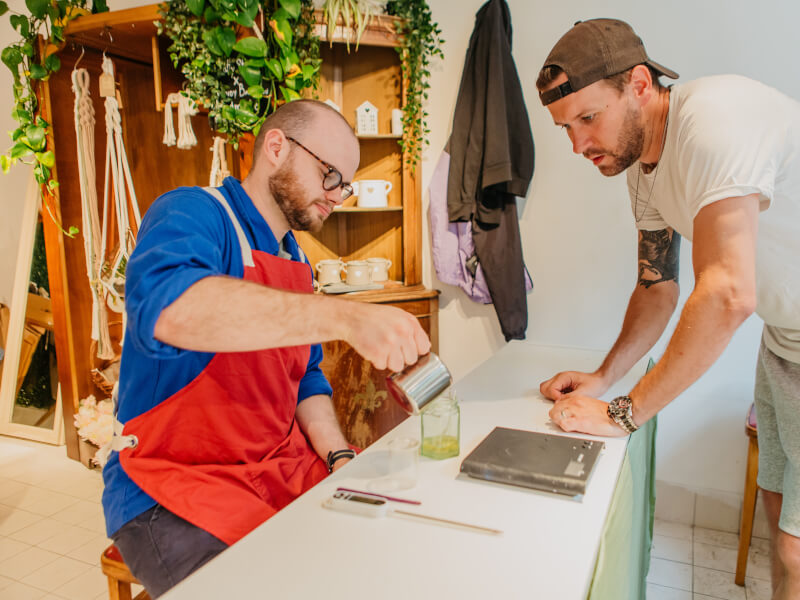 A man is teaching another man to make candles at a soy candle class