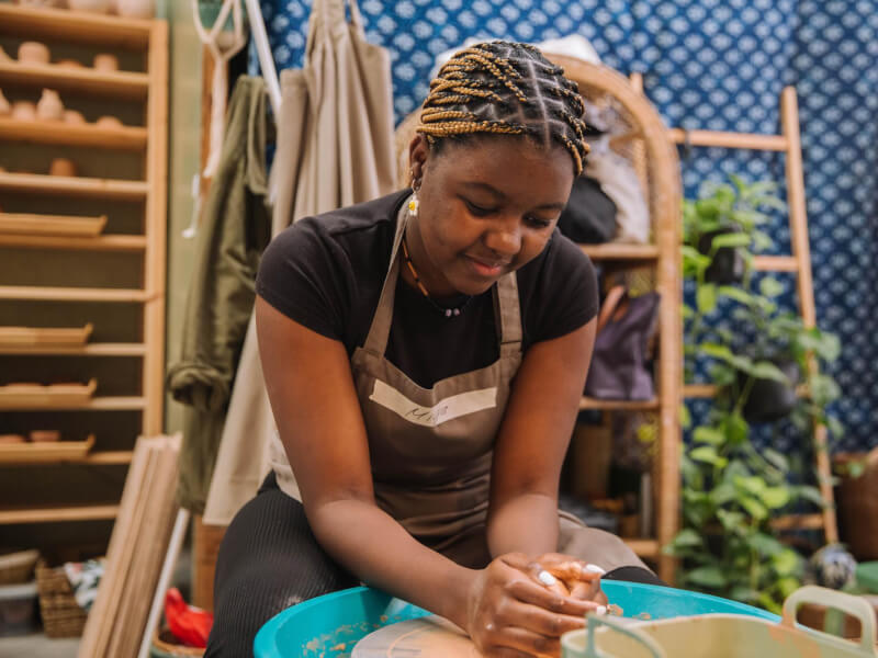 A woman with white nails begins throwing a clay pot on a wheel