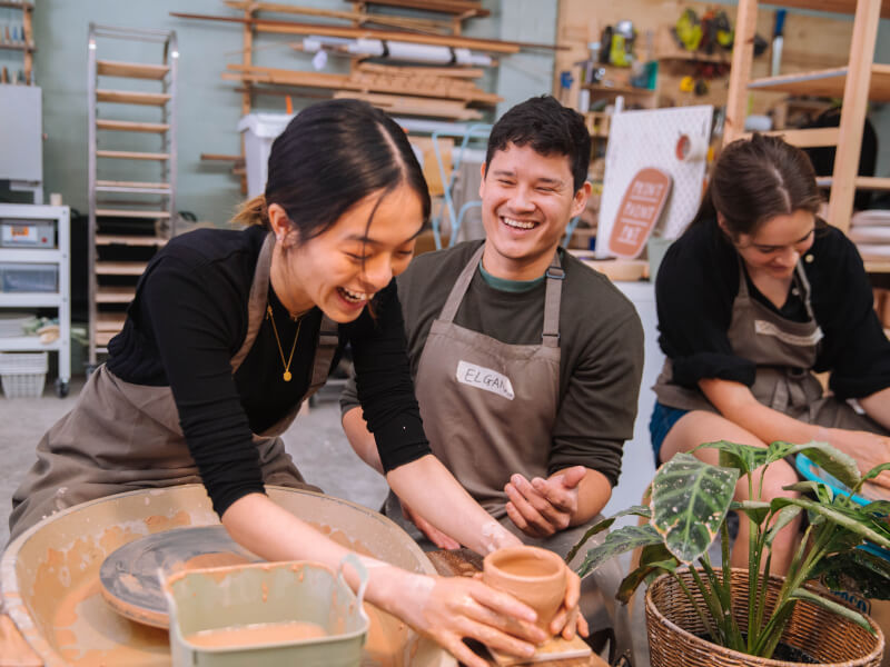 A couple making pottery at a wheel throwing class.