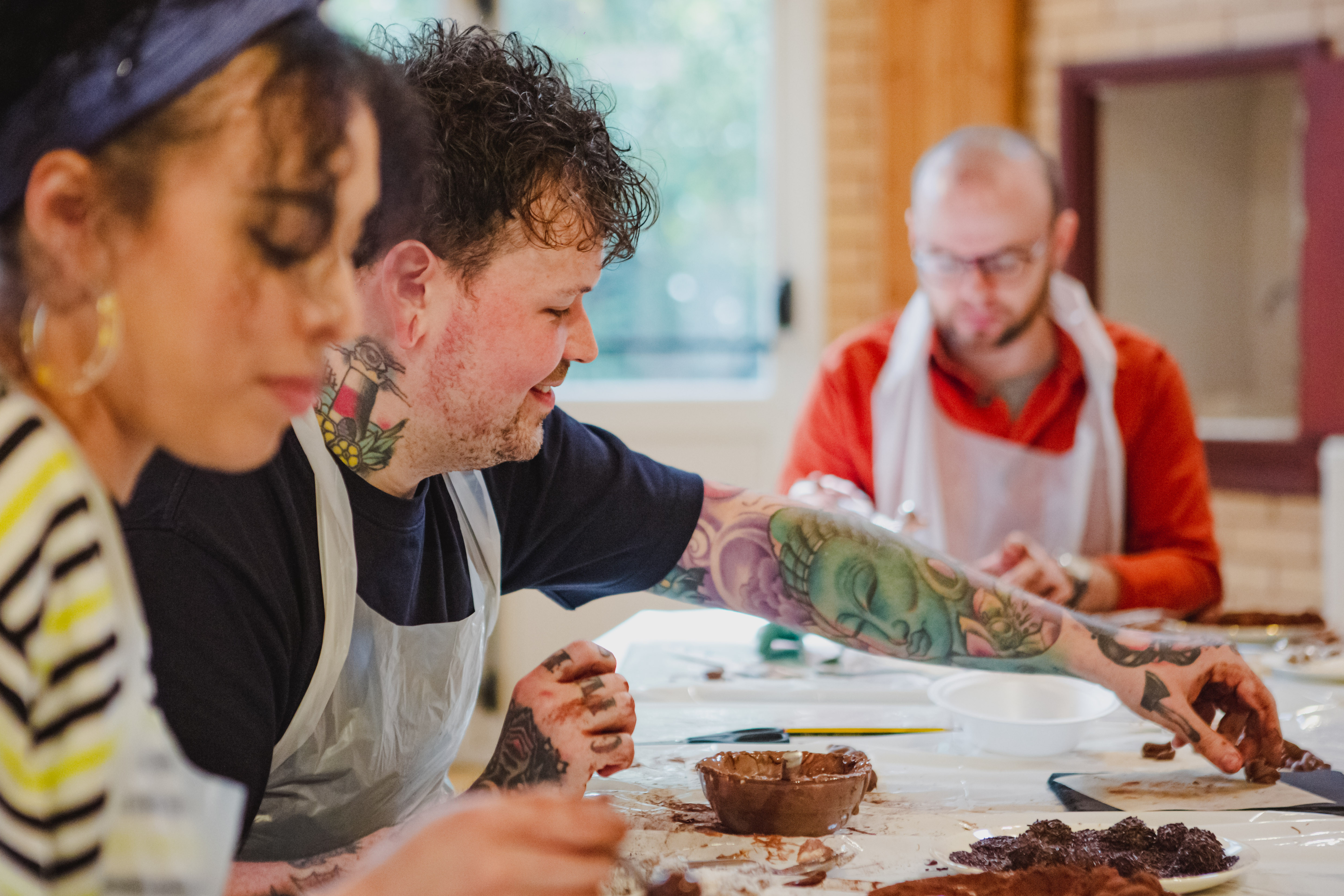 Three people at a table make chocolate truffles at a chocolate making class