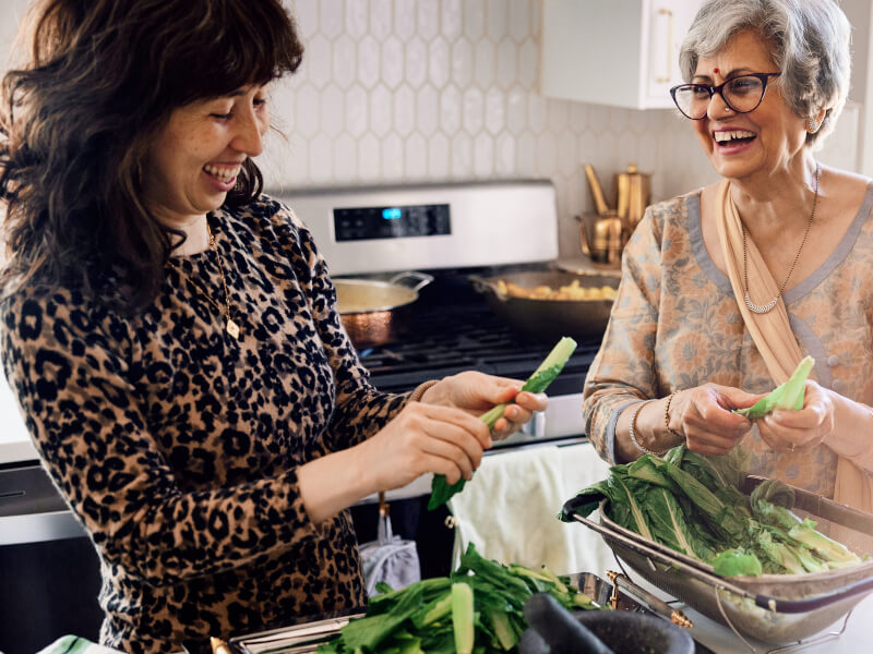 Two women are laughing and preparing green vegetables