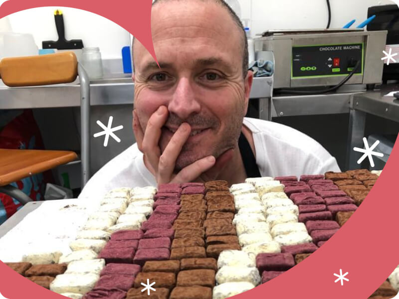 man smiling behind a tray of decorated chocolate truffles