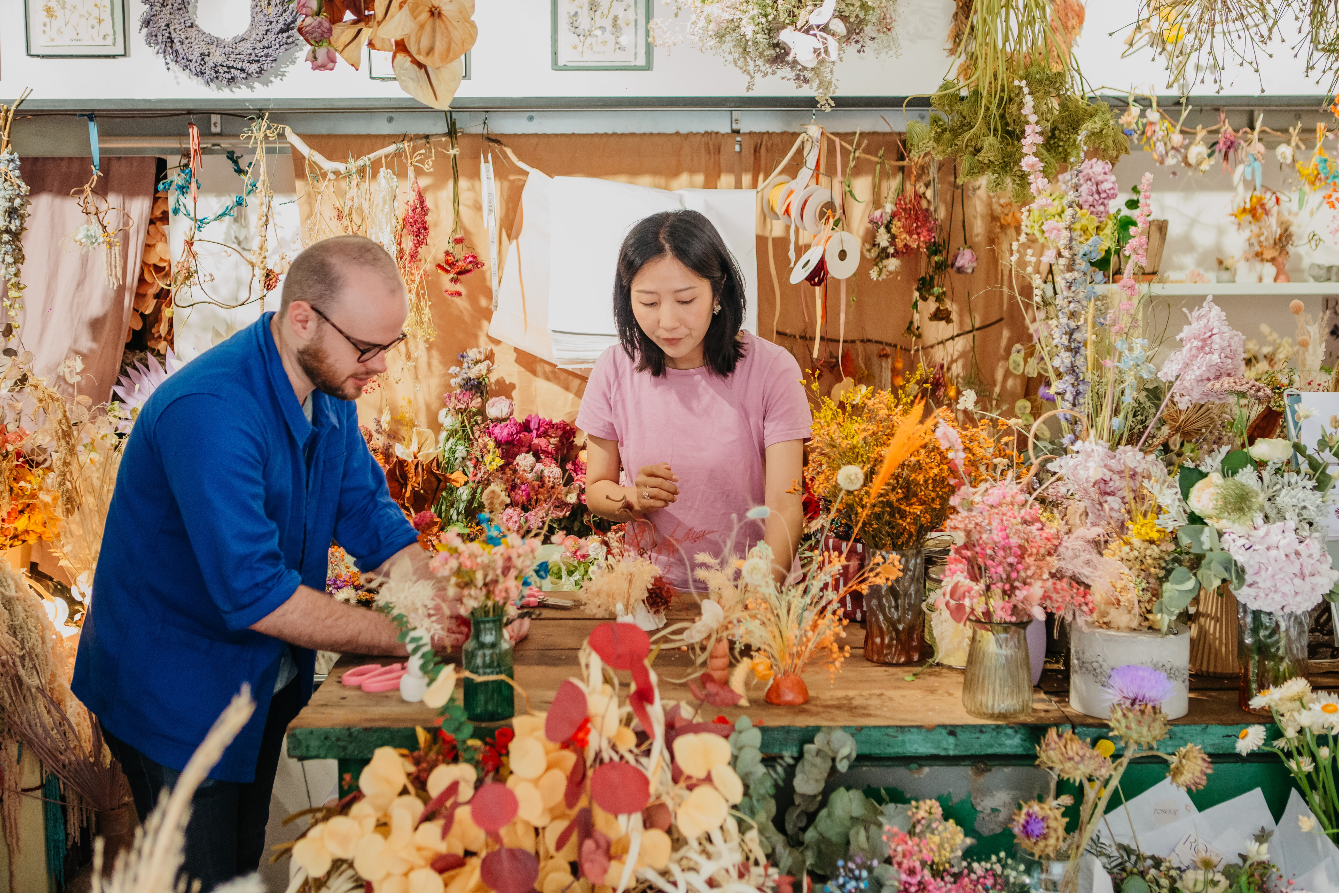 A teacher and a student working at a workshop surrounded by dried flowers