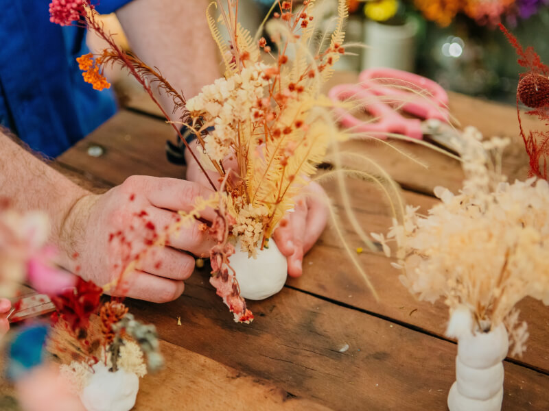 Close up of hands finishing an Ikebana flower arrangement inserted into a round handmade clay flower stand