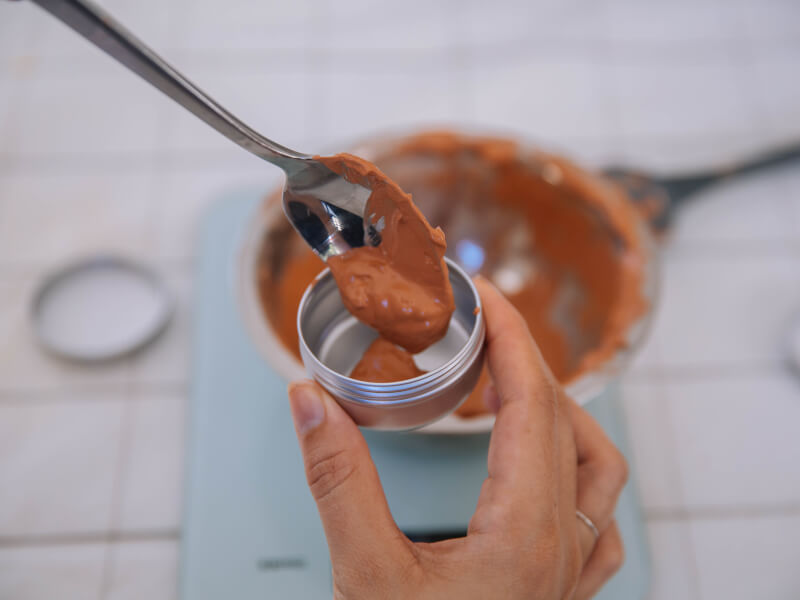 A close up of a person holding handmade make up in a small silver pot