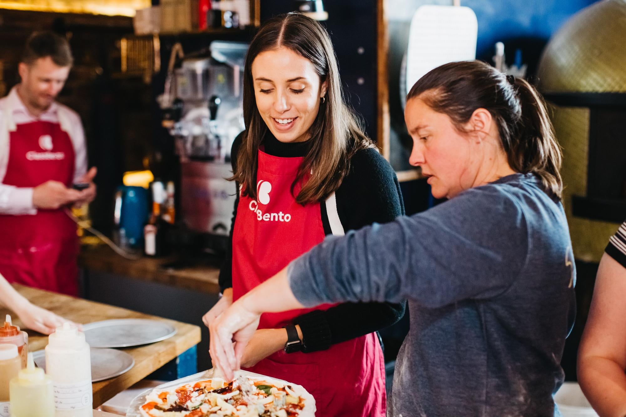A woman shows another woman how to make pizza at a pizza making class