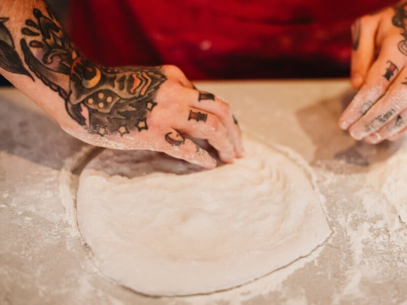 A man is making a pizza base by hand stretching the dough.