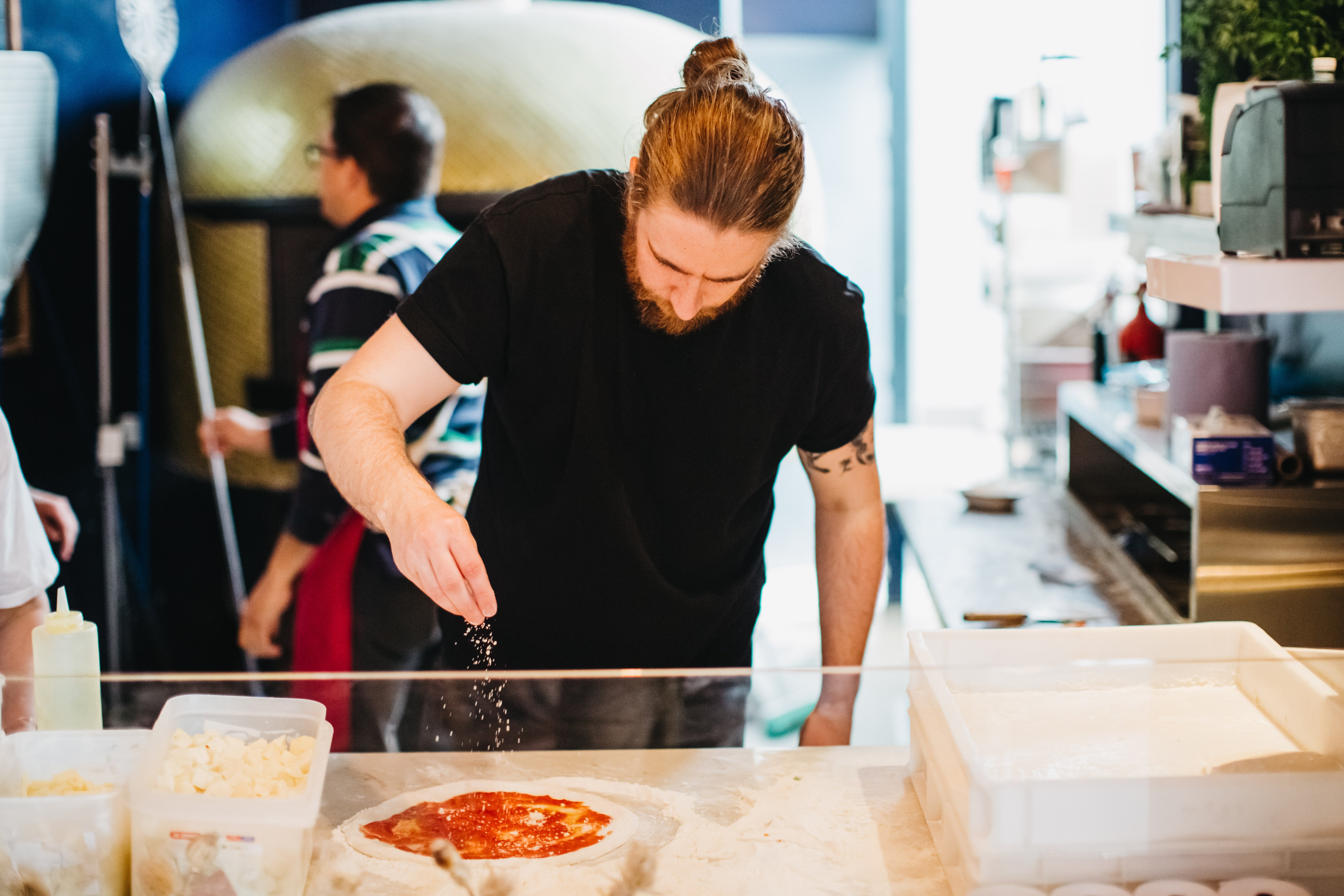 A man in a black t-shirt assembling an authentic Italian pizza