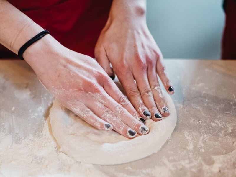 Close up of hands with painted nails kneading pizza dough