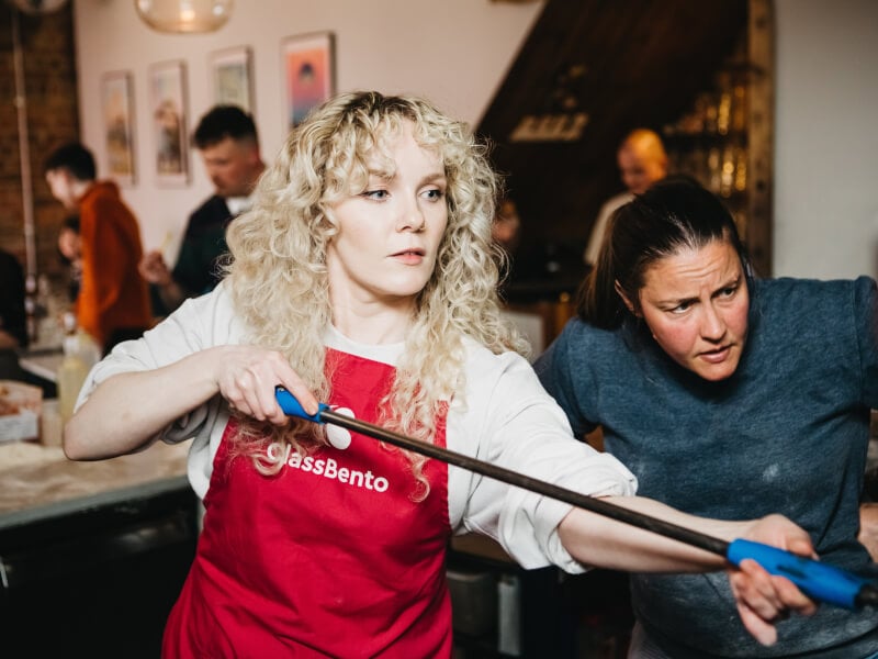 Woman wearing apron making pizza in a pizza oven.