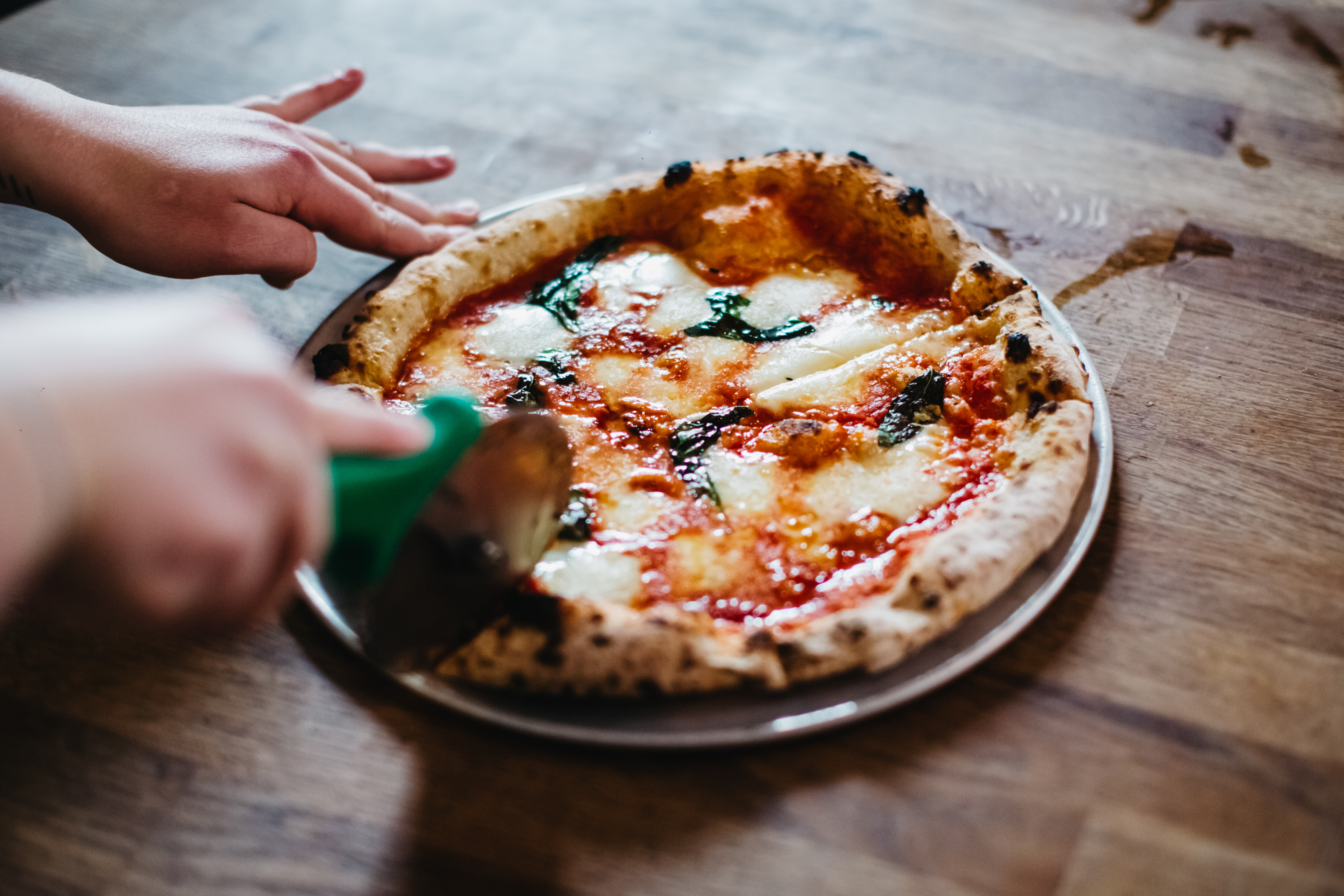 Close up of someone cutting a finished Neapolitan pizza with a rotary pizza cutter