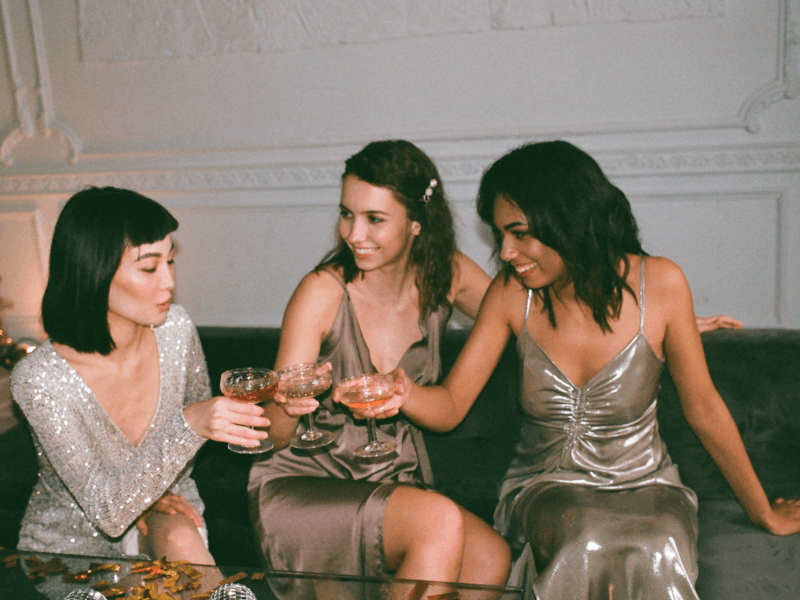 Three friends sitting down and clinking their cocktail glasses together.