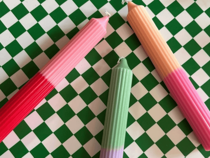 Three Habit Haus colour block candles in bright tones lie on a green checkerboard table cloth
