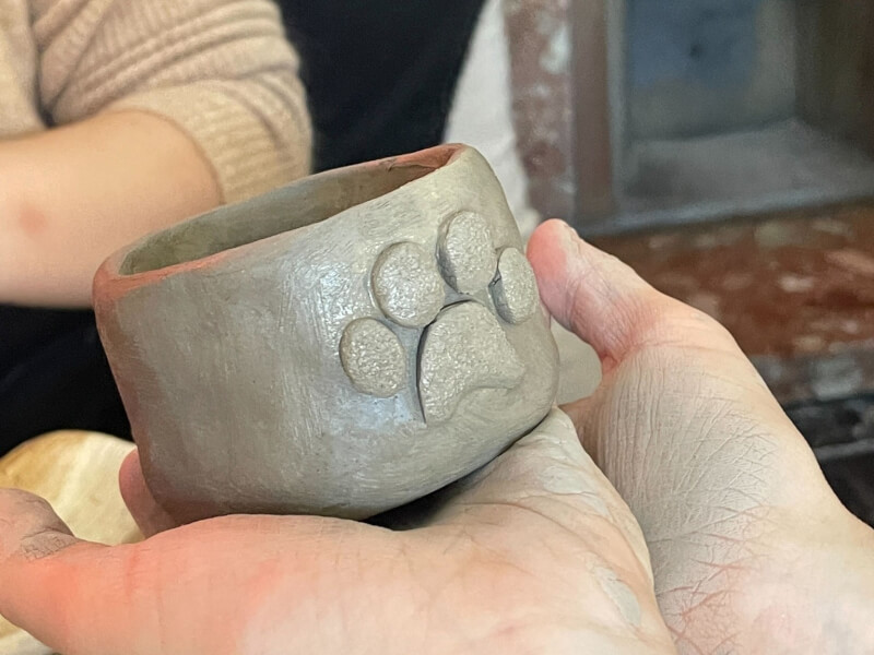 A close up of a handmade clay pot with a paw print embellishment on the side
