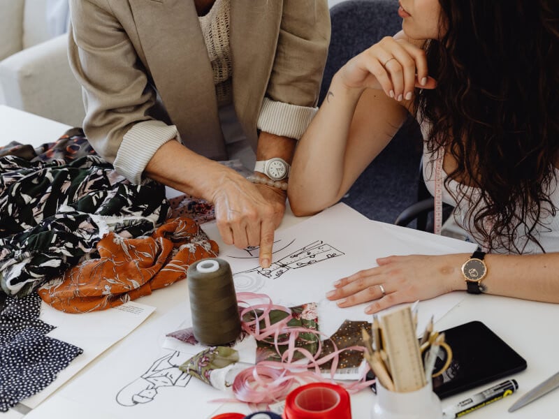 Two women look over fashion sewing patterns and ideas.