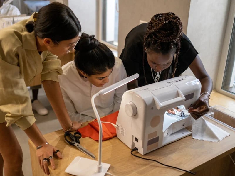 A group of women are working over a sewing machine in a sewing class.