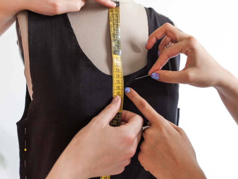 Two people are measuring and pinning fabric on a tailors dummy.