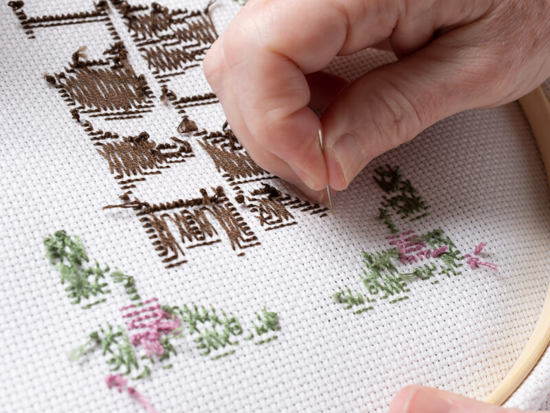 A person is embroidering a floral design on a piece of fabric in an embroidery hoop