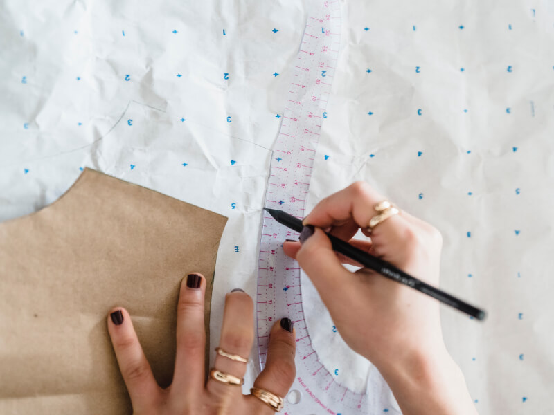 A close up of a person measuring and drawing a sewing pattern