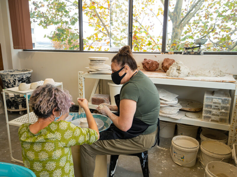 Teacher helping a student at a wheel throwing pottery class