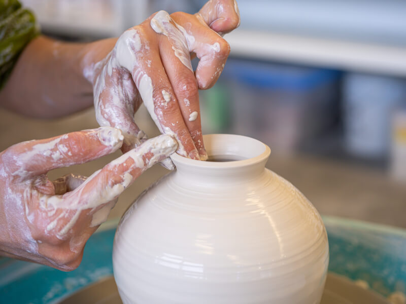A close up of two hands making a clay pot on a pottery wheel