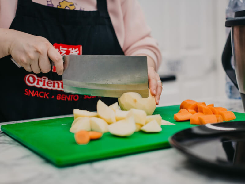 A person using a Chinese cleaver to slice up fruit on a green cutting board