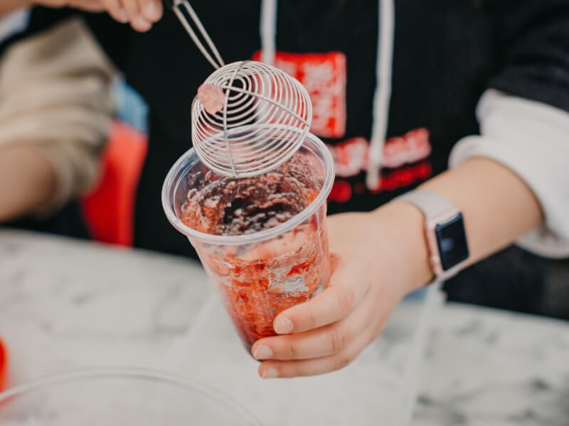 A close up of a person adding jelly pieces to red bubble tea