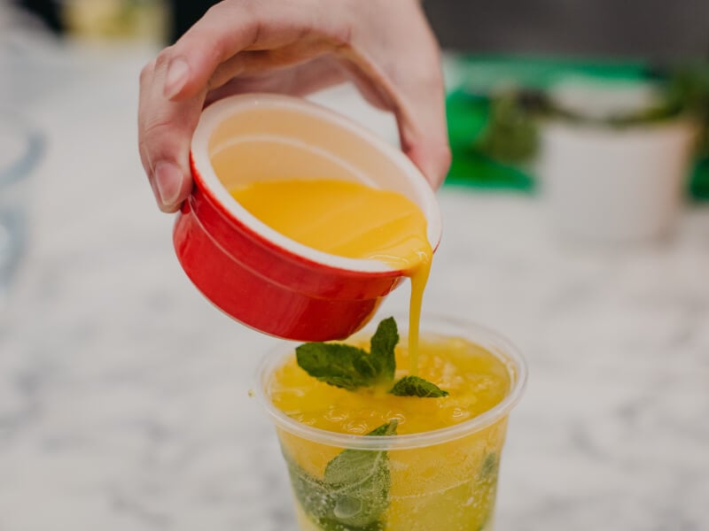 Person pouring fruit tea into a red plastic cup filled with ingredients