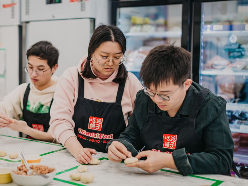 A teacher shows a couple how to make Chinese buns in a cooking course.