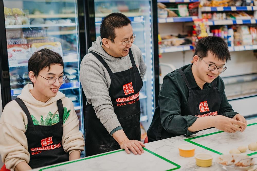 Three people laughing and talking at a cooking class