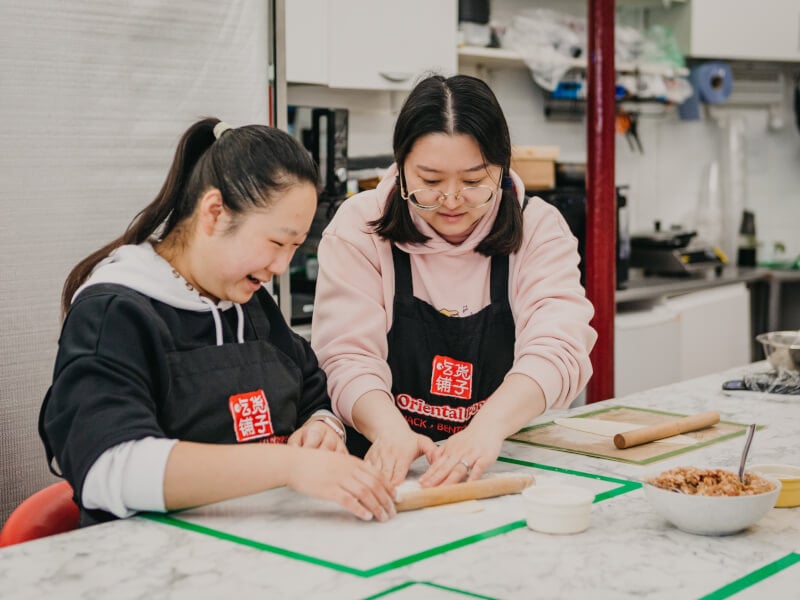 Teacher helping a cookery student to shape dough in a dumpling making class