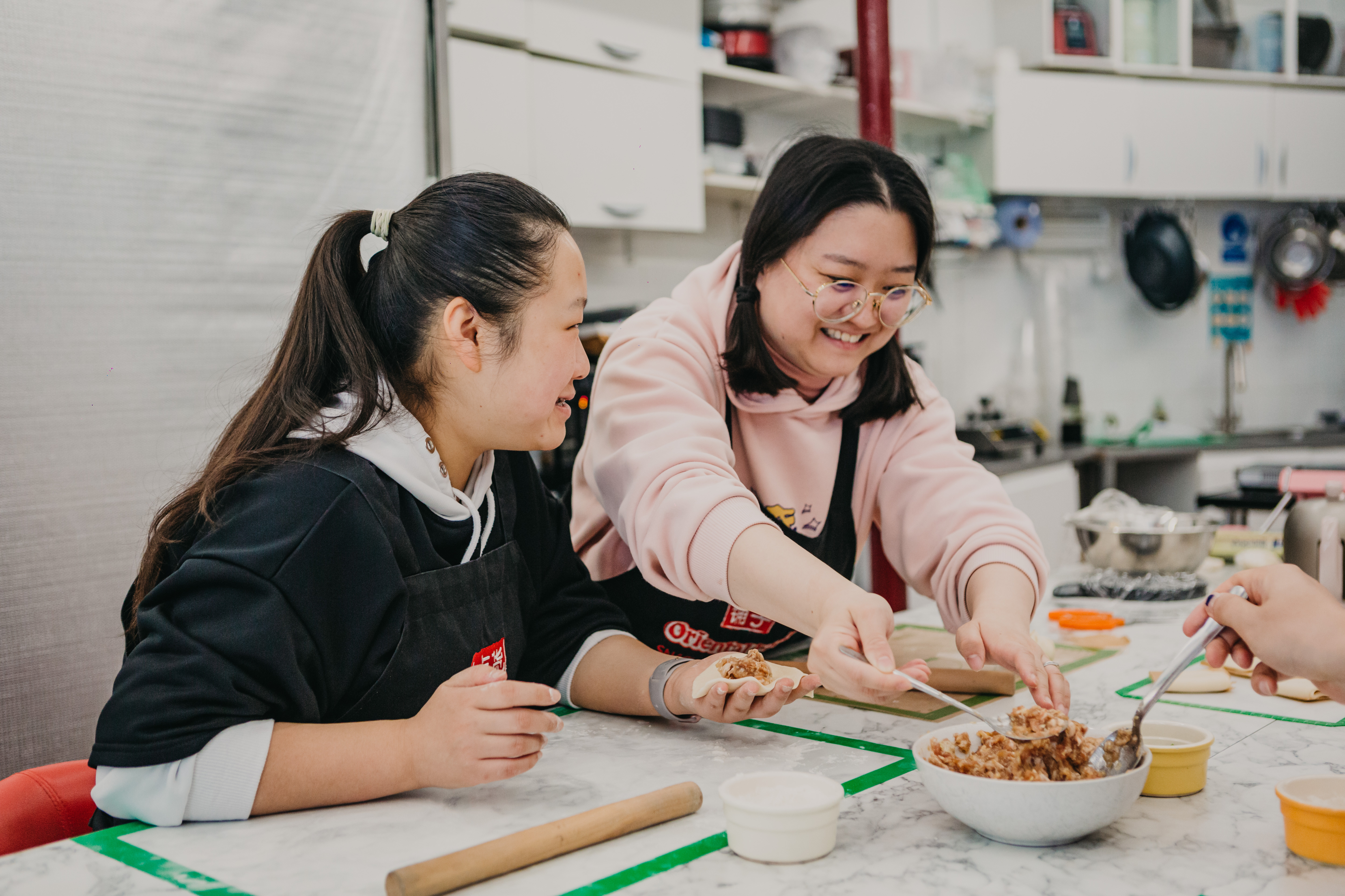 A pair of women are smiling and laughing at a cooking class