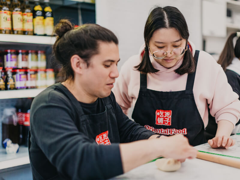 A woman teaching a man to cook Chinese dumplings at a cooking class