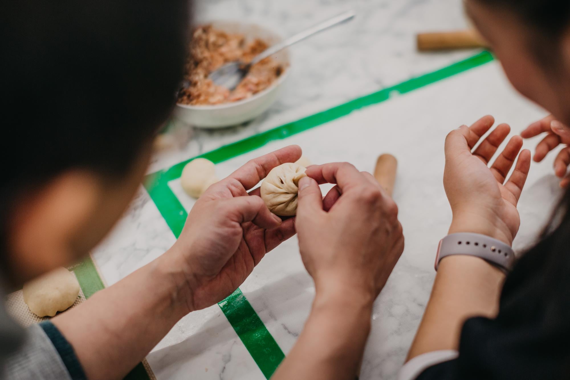 Two people shape Chinese dumplings by hand, shot from behind