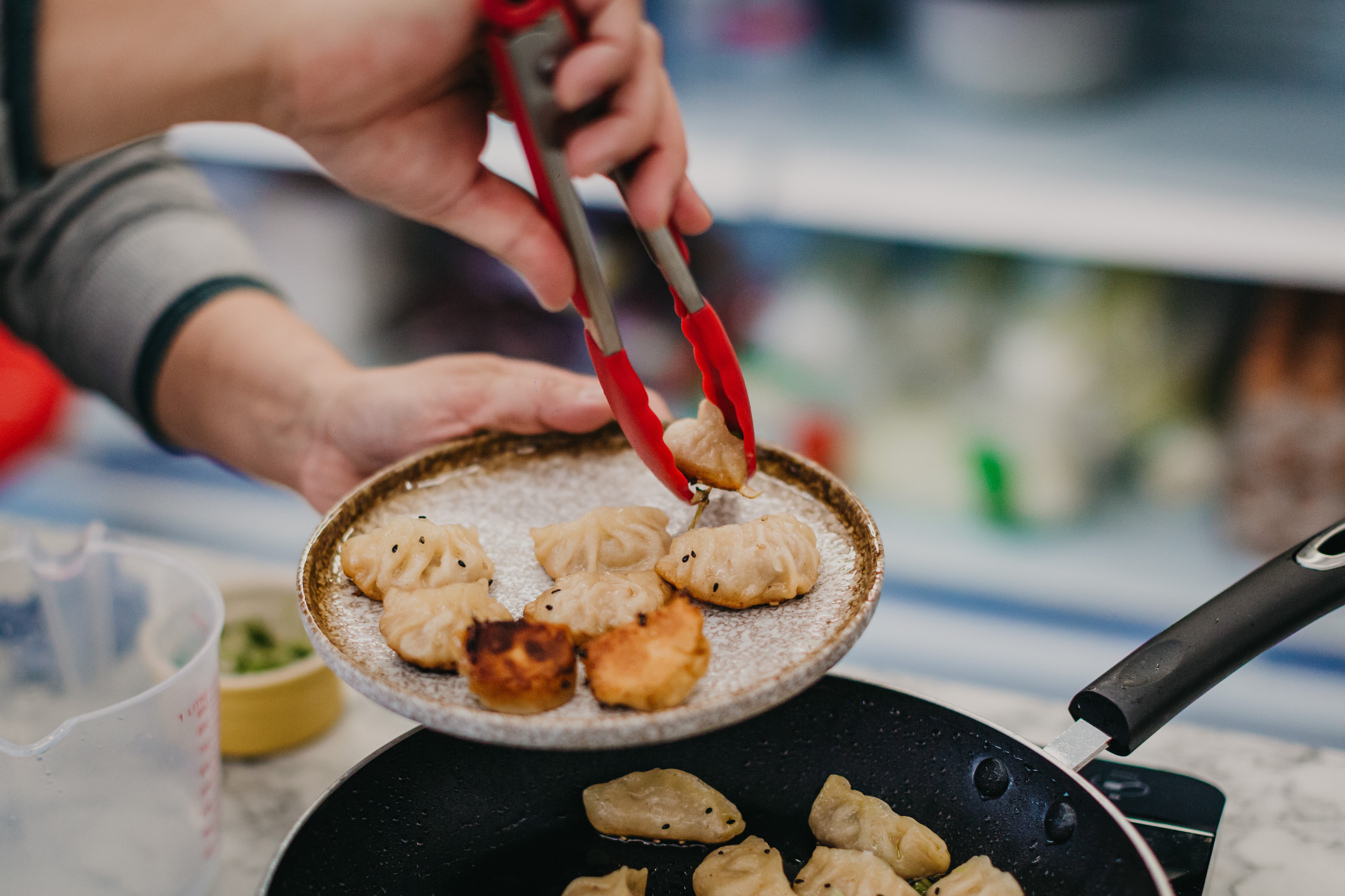 Person using tongs to remove Chinese dumplings from a frying pan