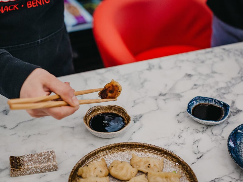 A person dips handmade Asian dumplings into sauce.