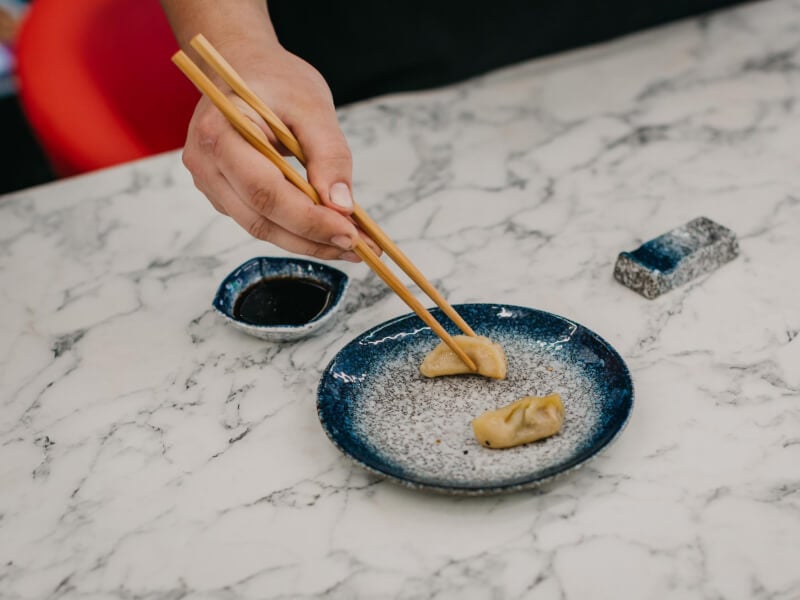 Hands picking up a small dumpling from a plate using chopsticks