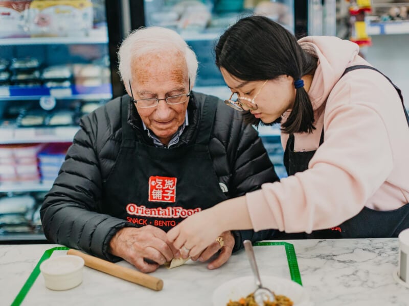 A woman helping an older man at a cooking class